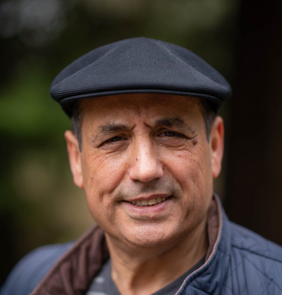 Dr. Younes Alila smiles at the camera wearing a black pageboy hat.